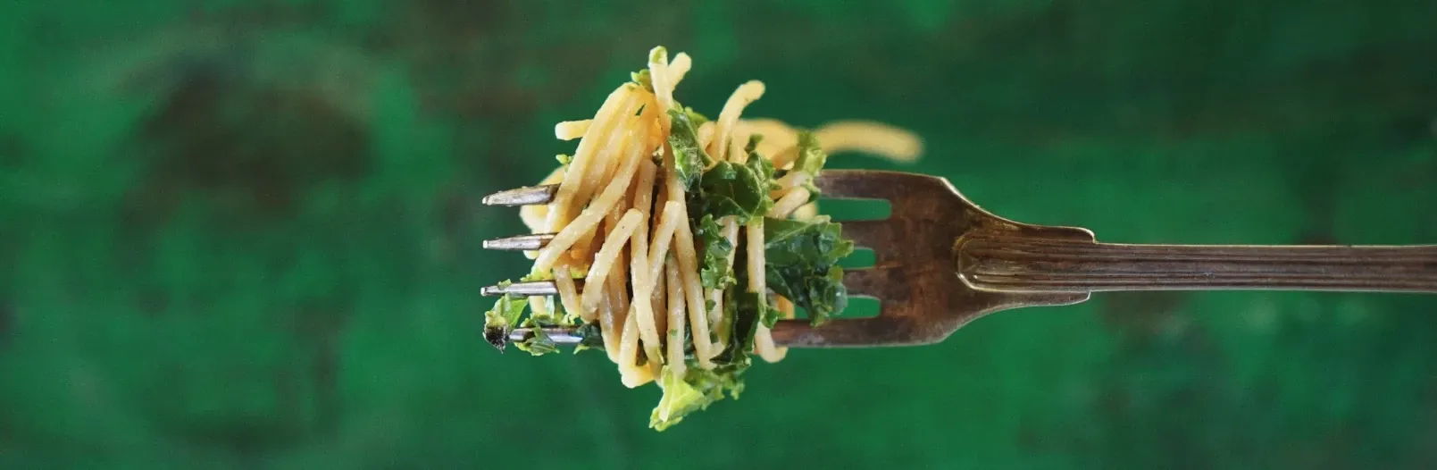 Des spaghettis enroulés sur une fourchette, sur fond vert